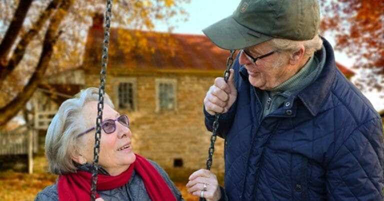 An older couple talking together on a garden swing in autumn